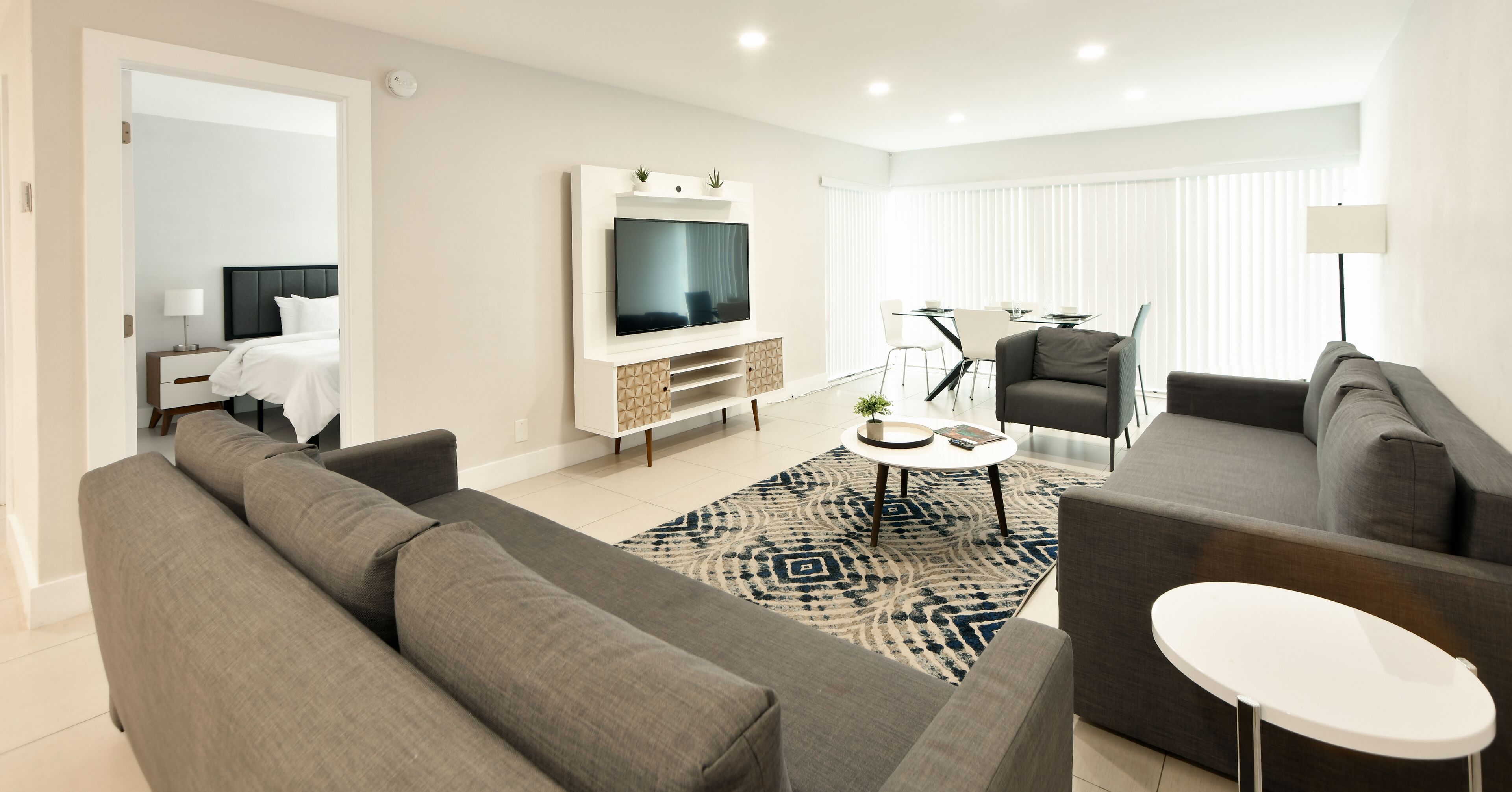 A modern living room with a grey sofa, a white coffee table, and a flat-screen TV mounted on the wall.