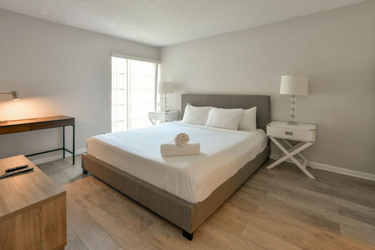 A modern hotel room with a large bed, a desk, and a nightstand with lamps.