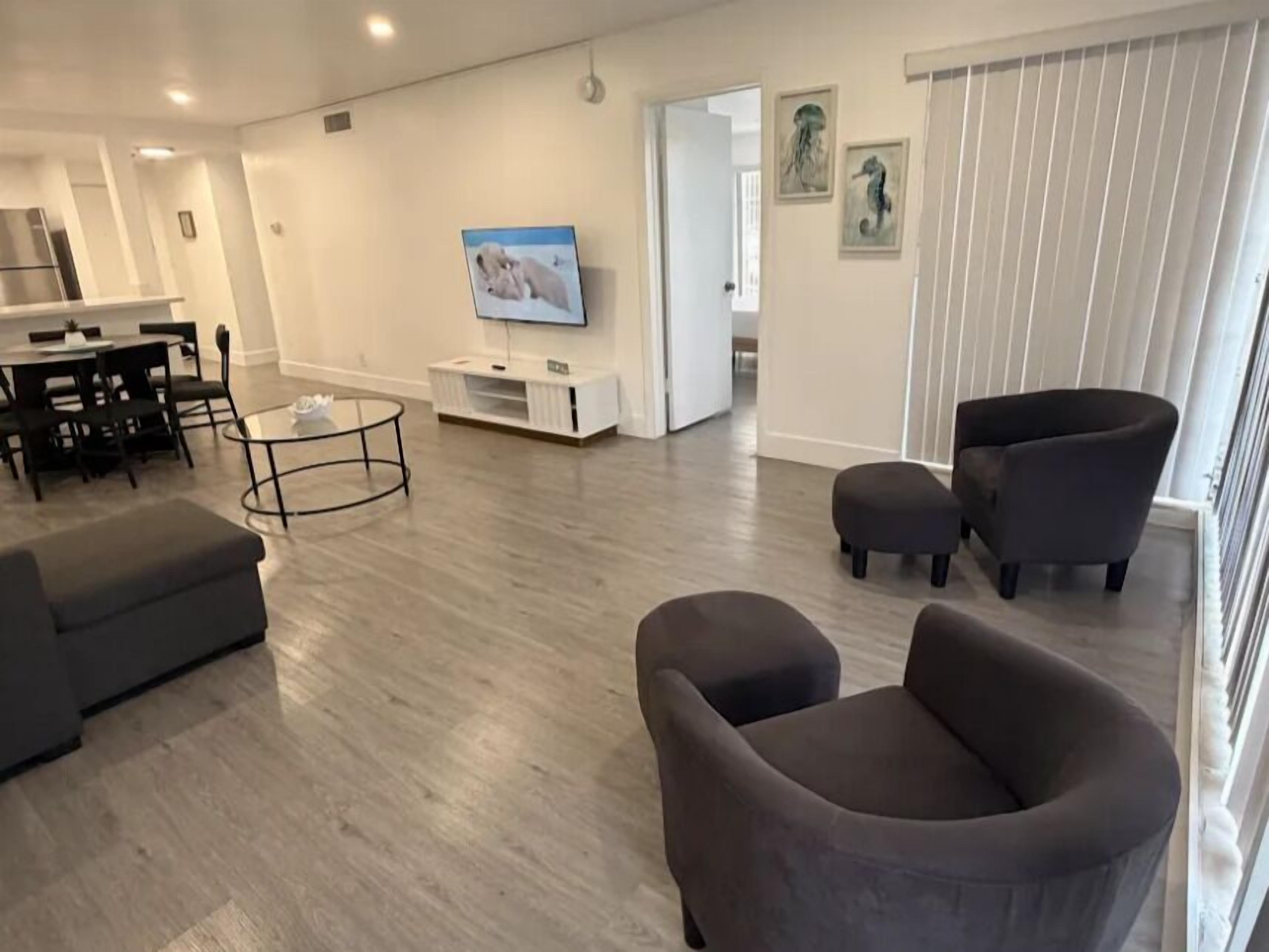 A modern living room with a dining area, a TV, and a balcony with blinds.