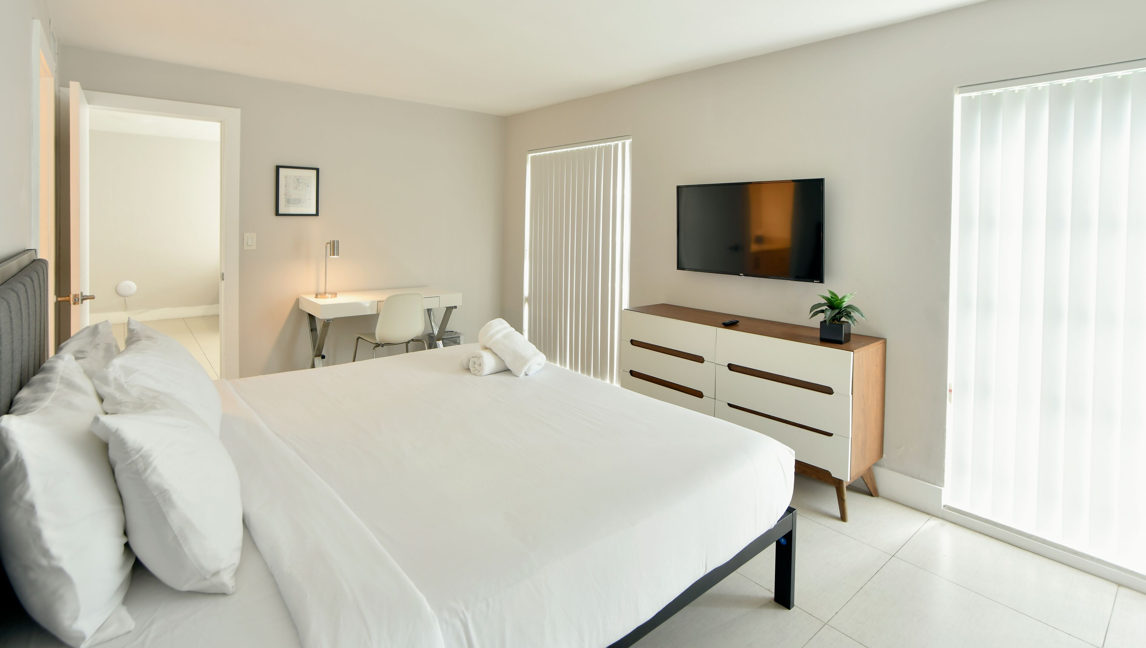 Een moderne hotelkamer met een groot bed, een bureau, een stoel, een televisie en een raam met jaloezieën.