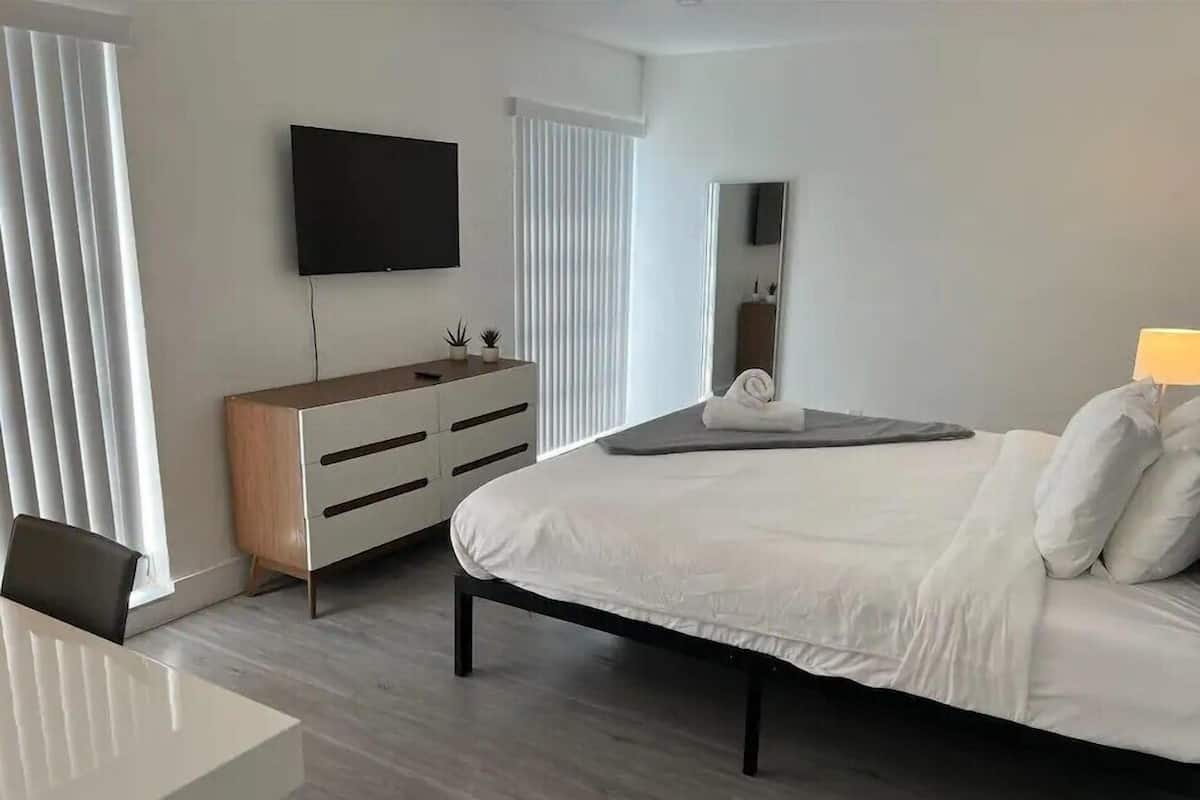 A modern hotel room with a bed, a TV mounted on the wall, a dresser, and a desk.