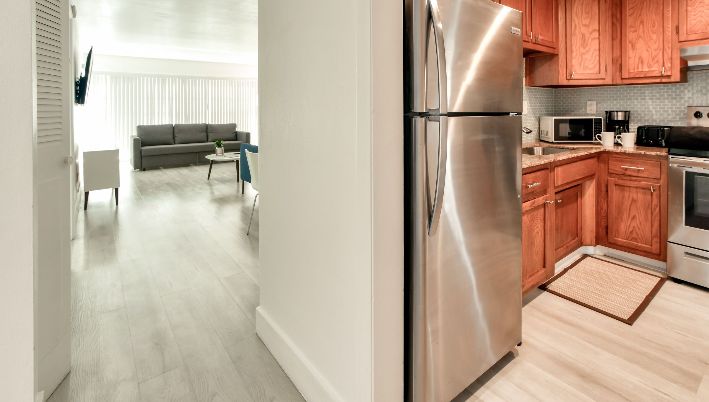 A modern kitchen with stainless steel appliances, wooden cabinets, and a grey tiled backsplash.