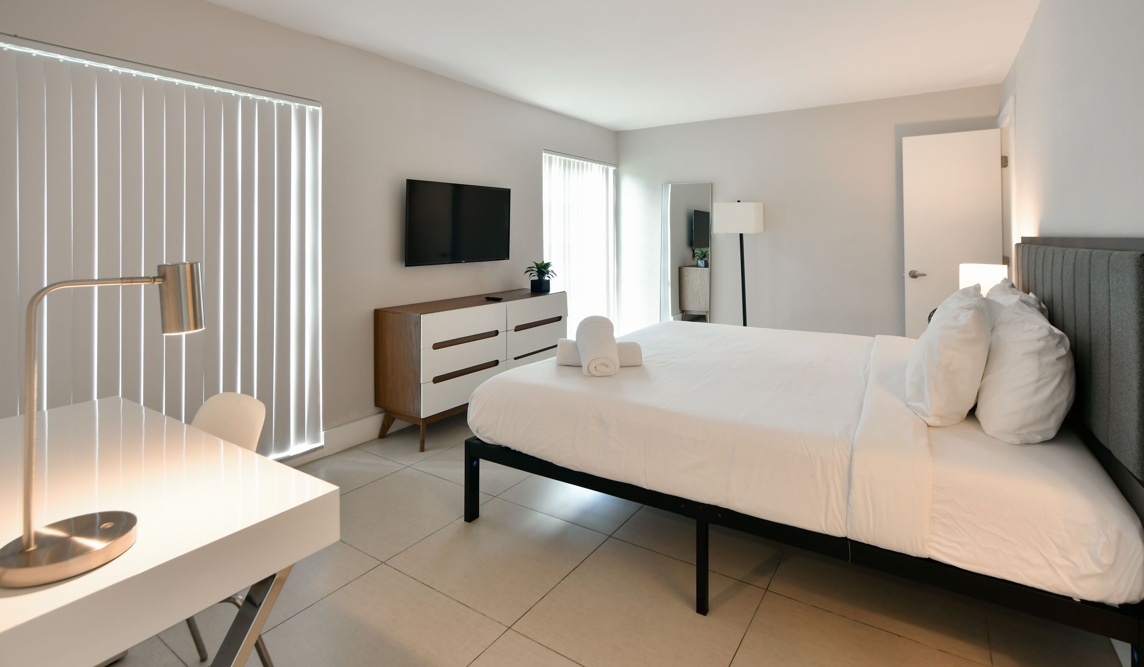 Een moderne hotelkamer met een bed, nachtkastje, televisie en een bureau met een lamp.