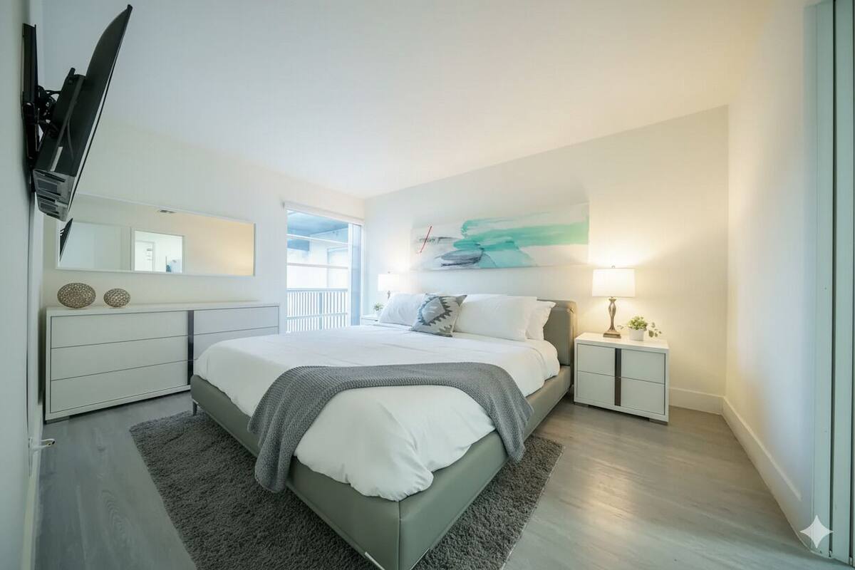 A modern bedroom with a large bed, bedside tables, a mirror, and a painting on the wall.