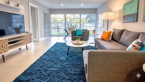 Un salon moderne avec un téléviseur à écran plat, un canapé, une table basse et un tapis bleu.