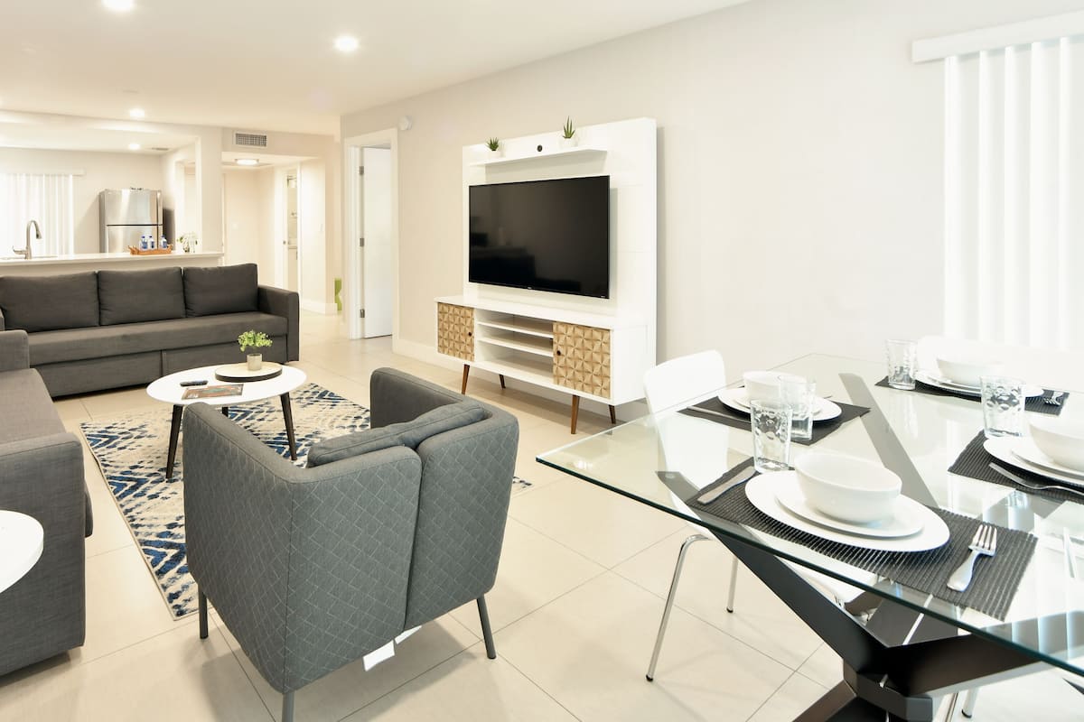 A modern living room with a sofa, armchair, coffee table, and a dining area with a glass table and chairs.