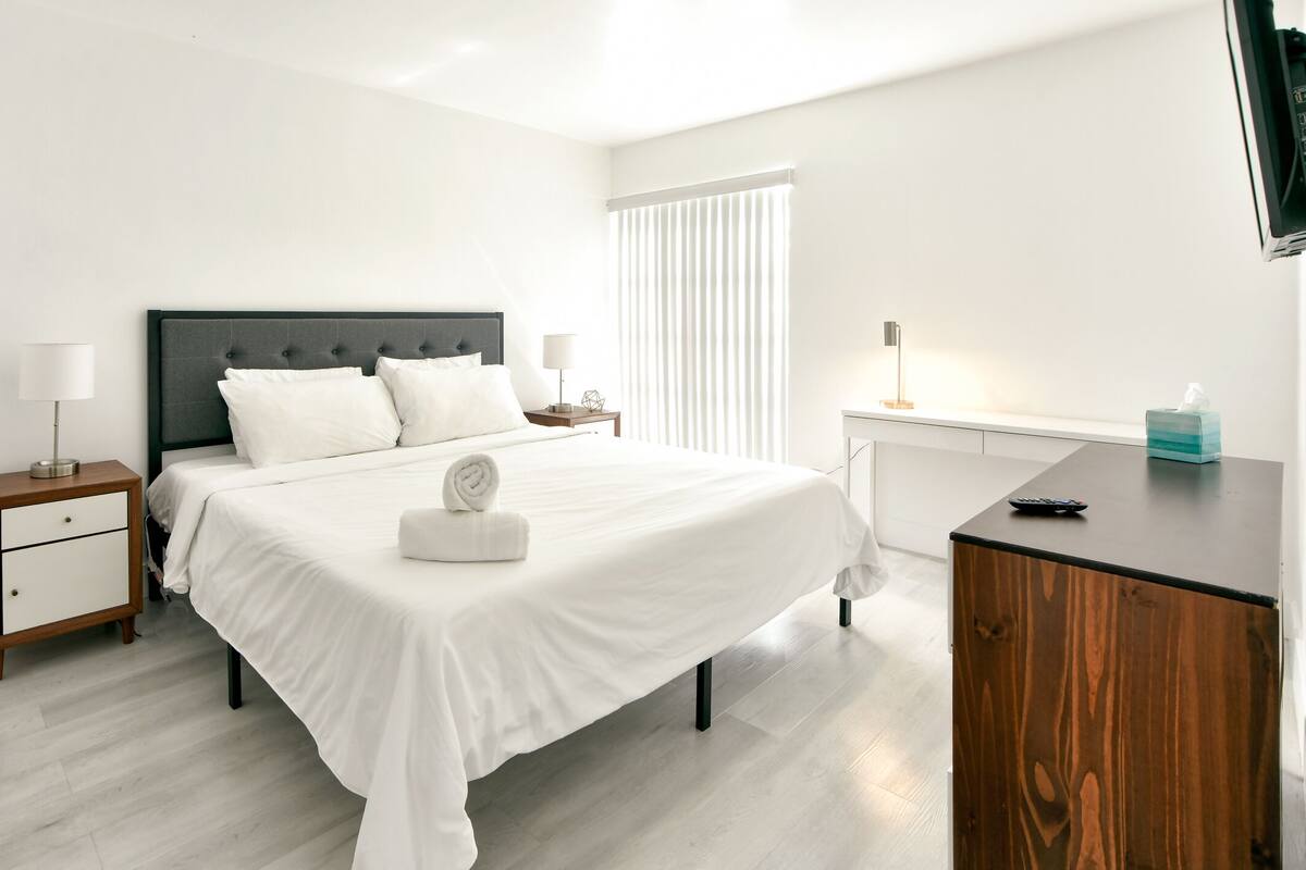 A neatly arranged hotel room with a bed, bedside tables, a desk, and a TV.