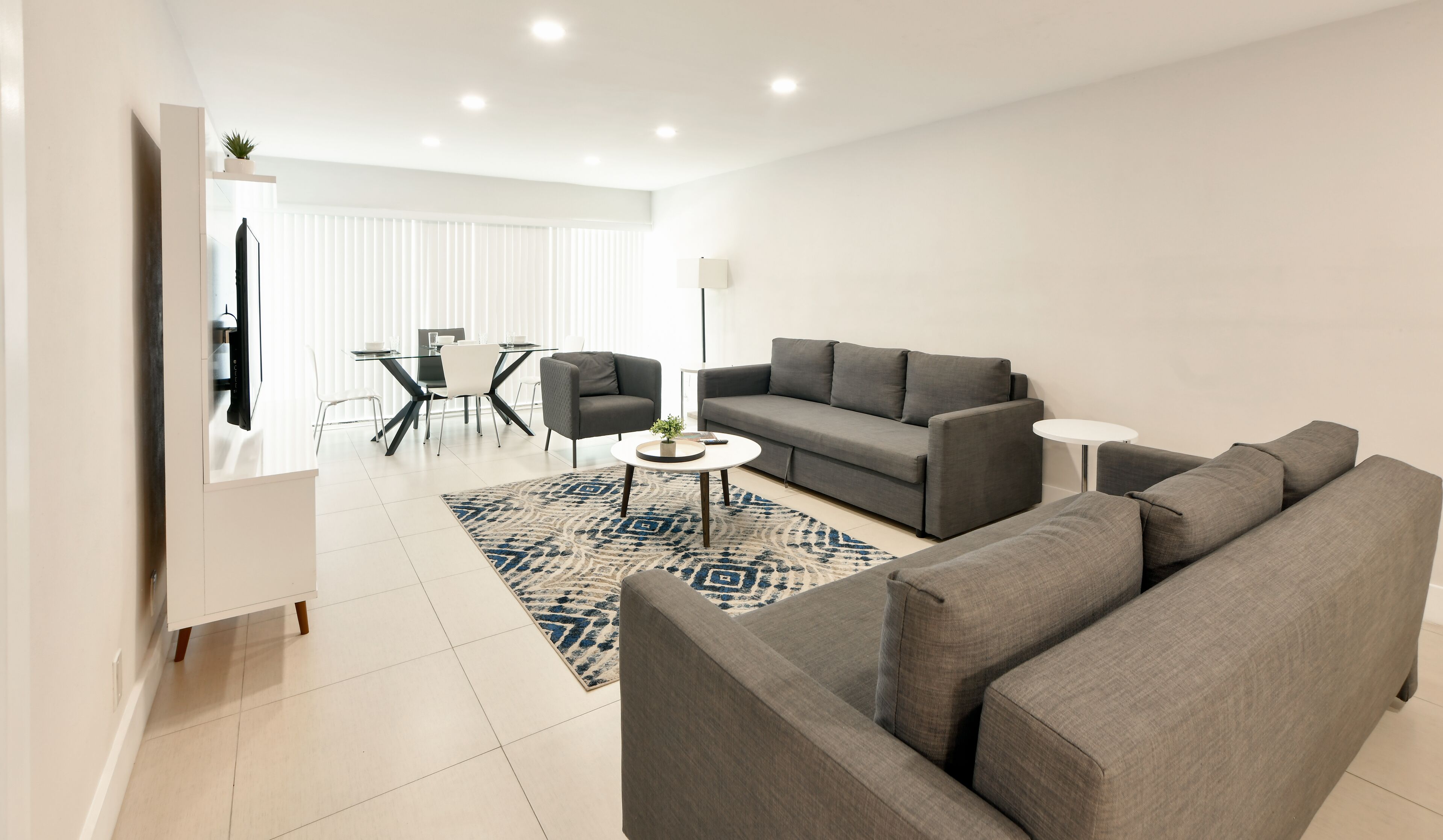A modern living room with a grey sofa, a round coffee table, and a dining area with a glass table and chairs.