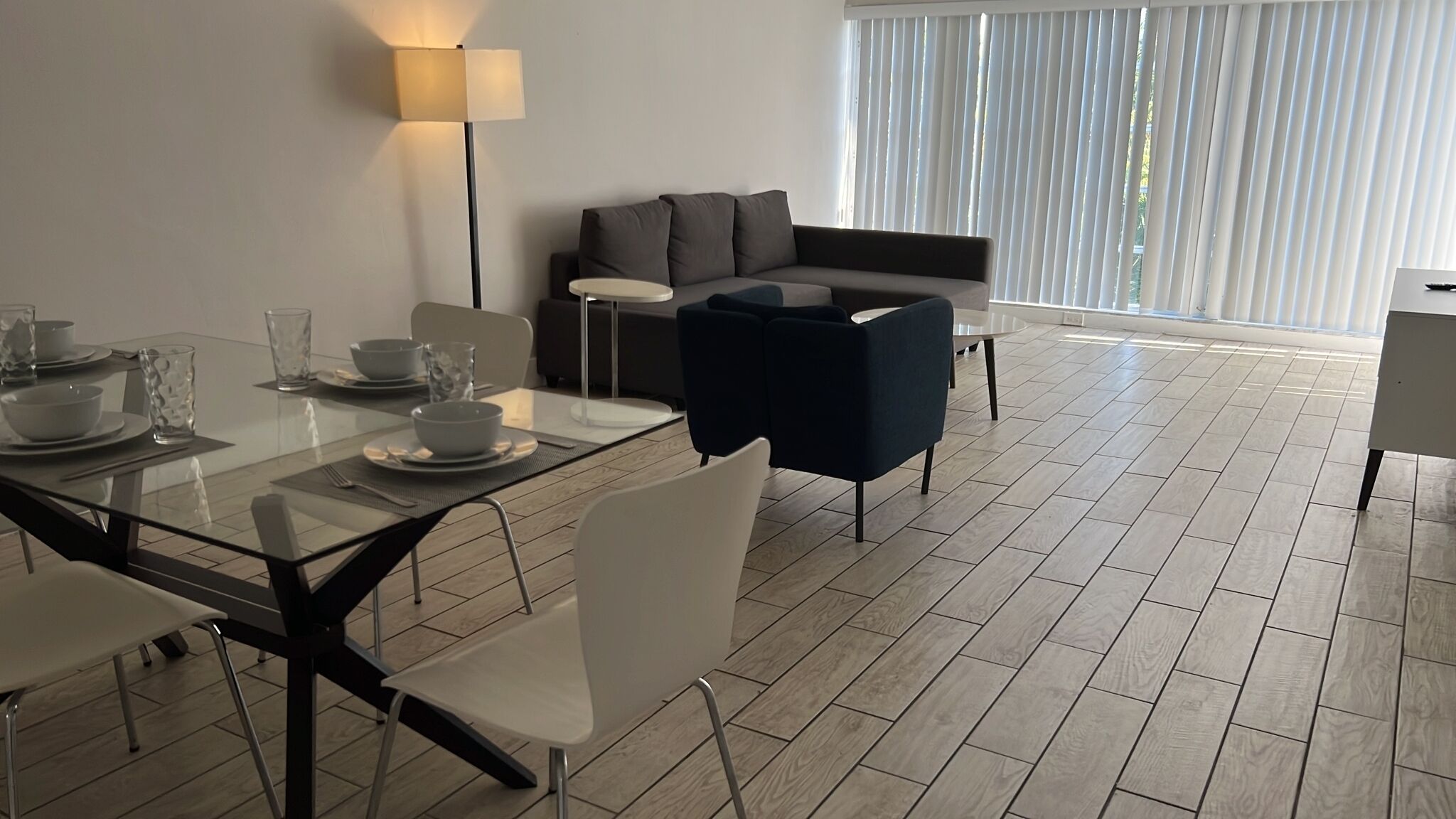 A modern living room with a sofa, a dining table set for two, and a floor lamp.