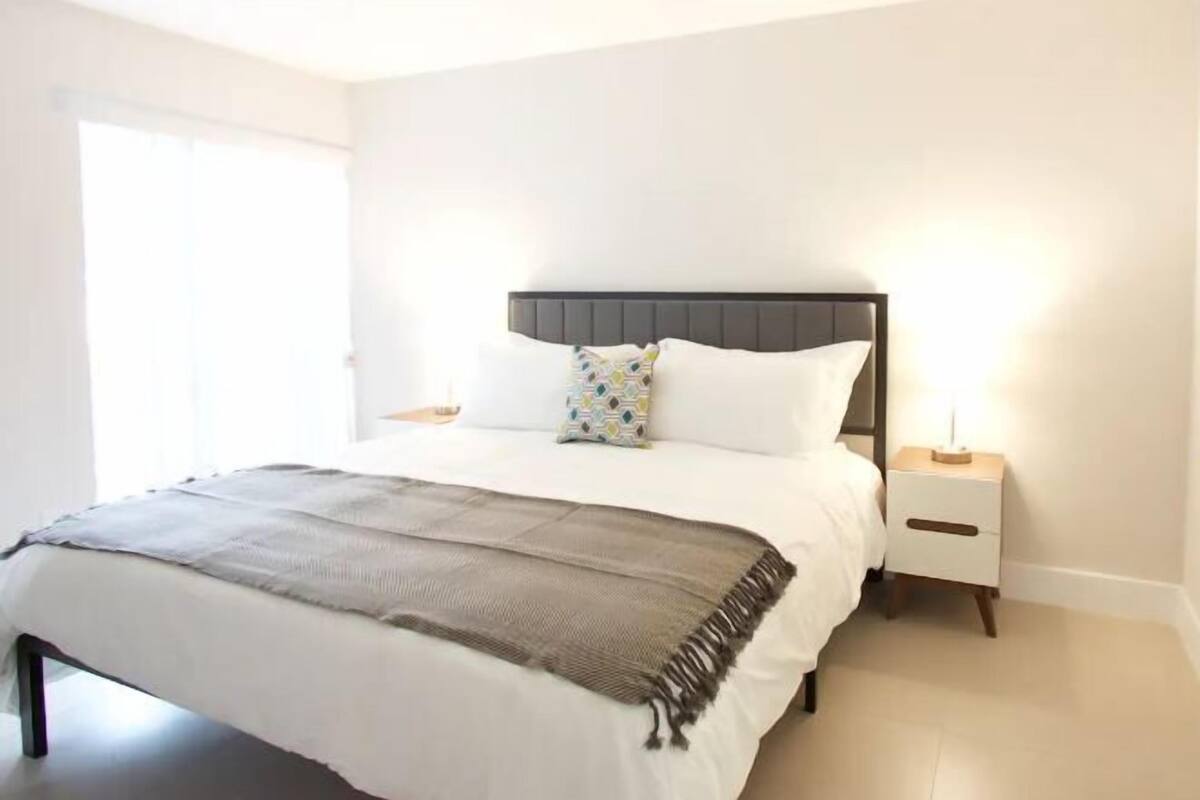 A bedroom with a bed, a bedside table, a nightstand, and a door.