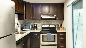 Une cuisine avec des meubles en bois foncé, des appareils en acier inoxydable, un plan de travail en granit et une fenêtre avec des stores.