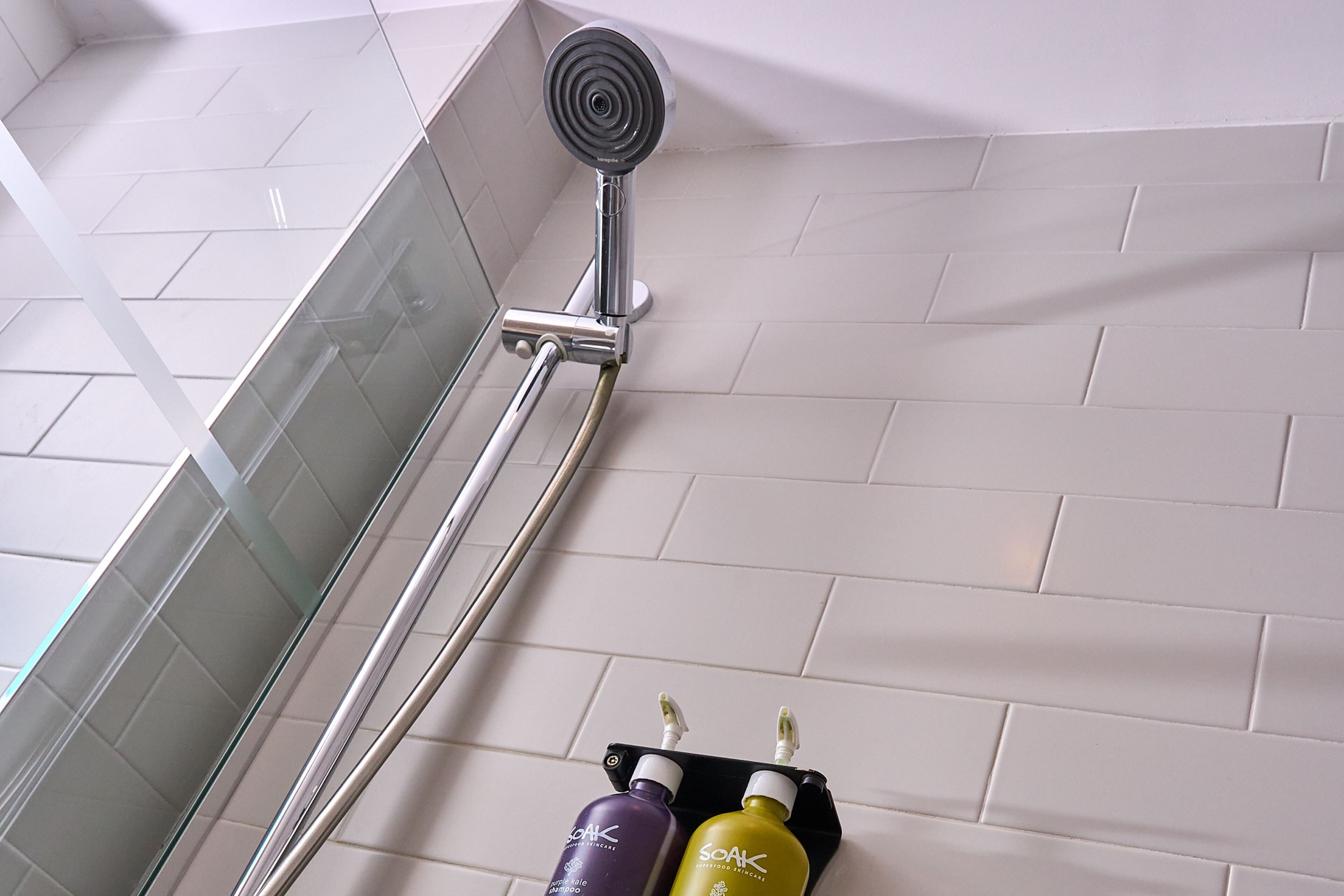 A shower area with a glass door, a handheld showerhead, and two bottles of shampoo in a black soap dish.