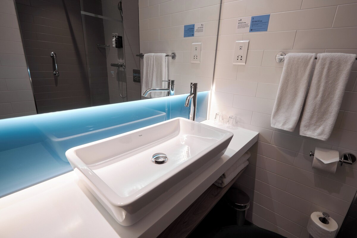 A modern bathroom with a white sink, blue bathtub, and a shower area.