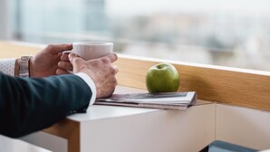 A person holding a cup, sitting at a table with a tablet and an apple. - Holiday Inn Express Malta by IHG (St. Julian's)