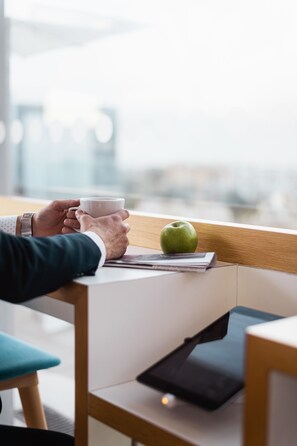 A person holding a cup, sitting at a table with a tablet and an apple. - Holiday Inn Express Malta by IHG (St. Julian's)