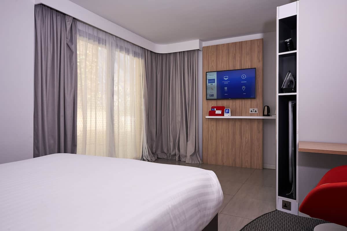 A modern hotel room with a large bed, a TV mounted on the wall, a desk with a computer, and a wardrobe.