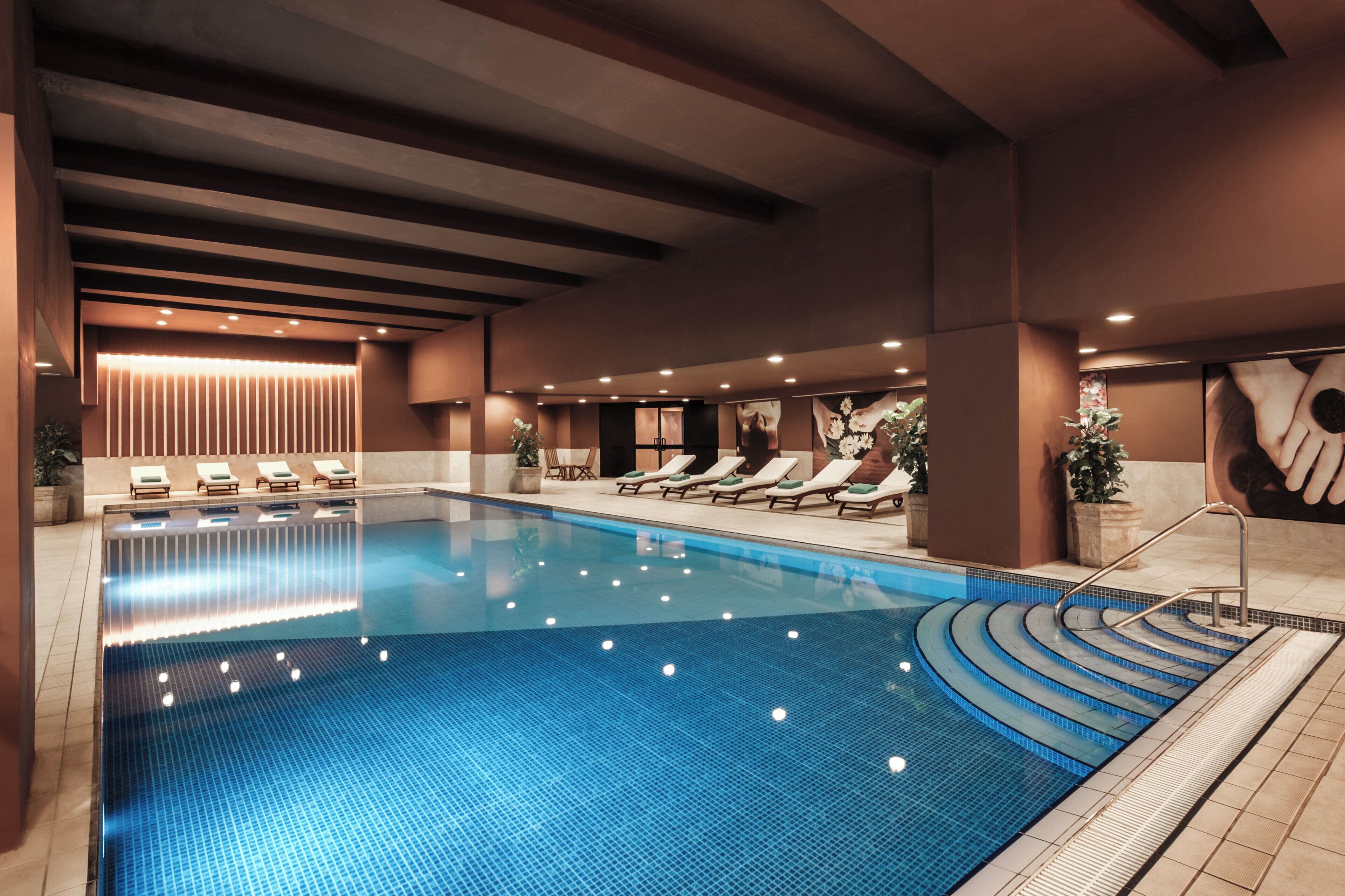 Una amplia piscina interior con numerosas tumbonas y un diseño de techo moderno.
