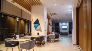 A modern dining area with tables and chairs, a large window with curtains, and a television in the background. - Holiday Inn Express Malta by IHG (St. Julian's)