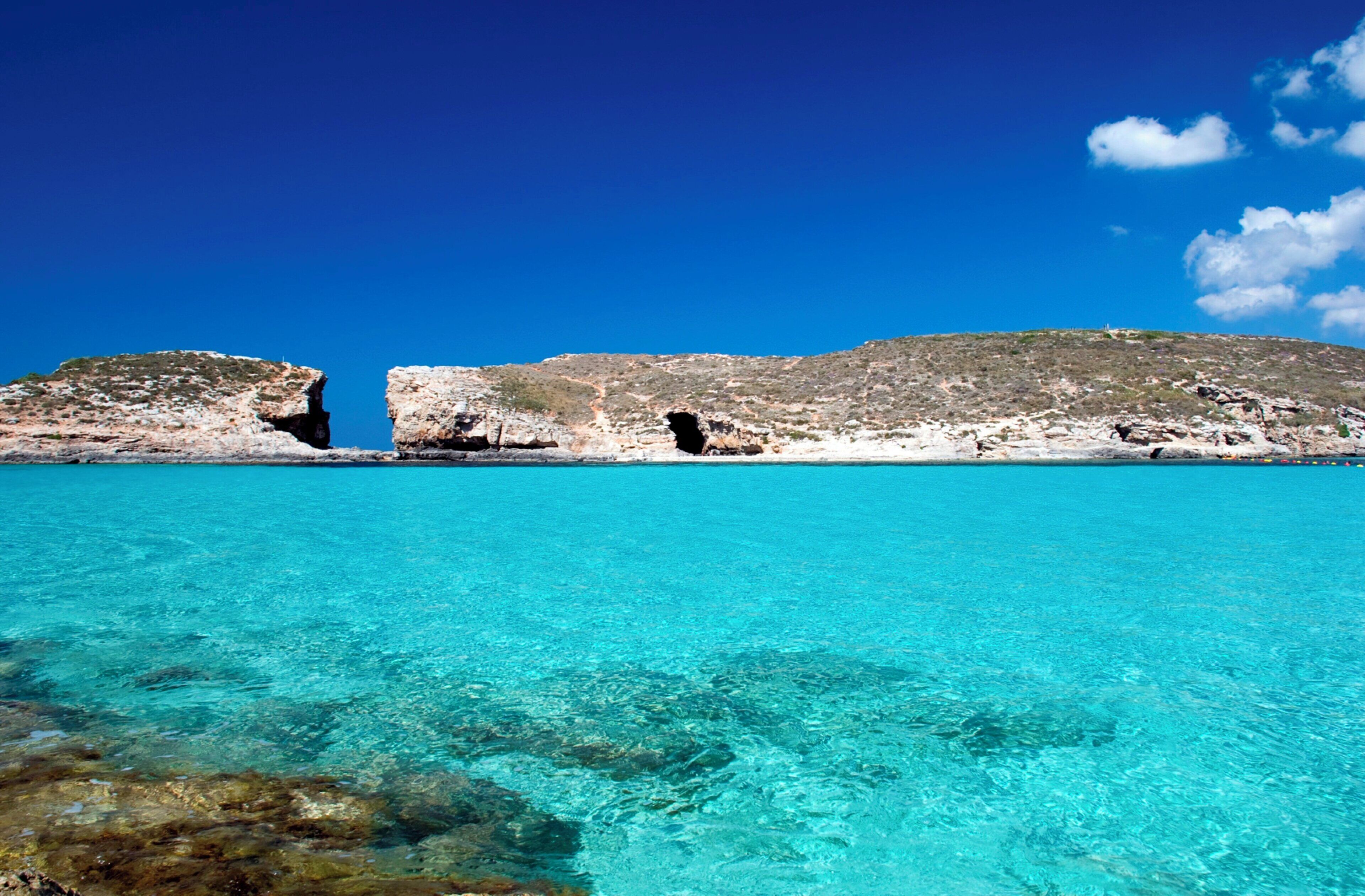 A clear turquoise sea with rocky formations and a clear sky.