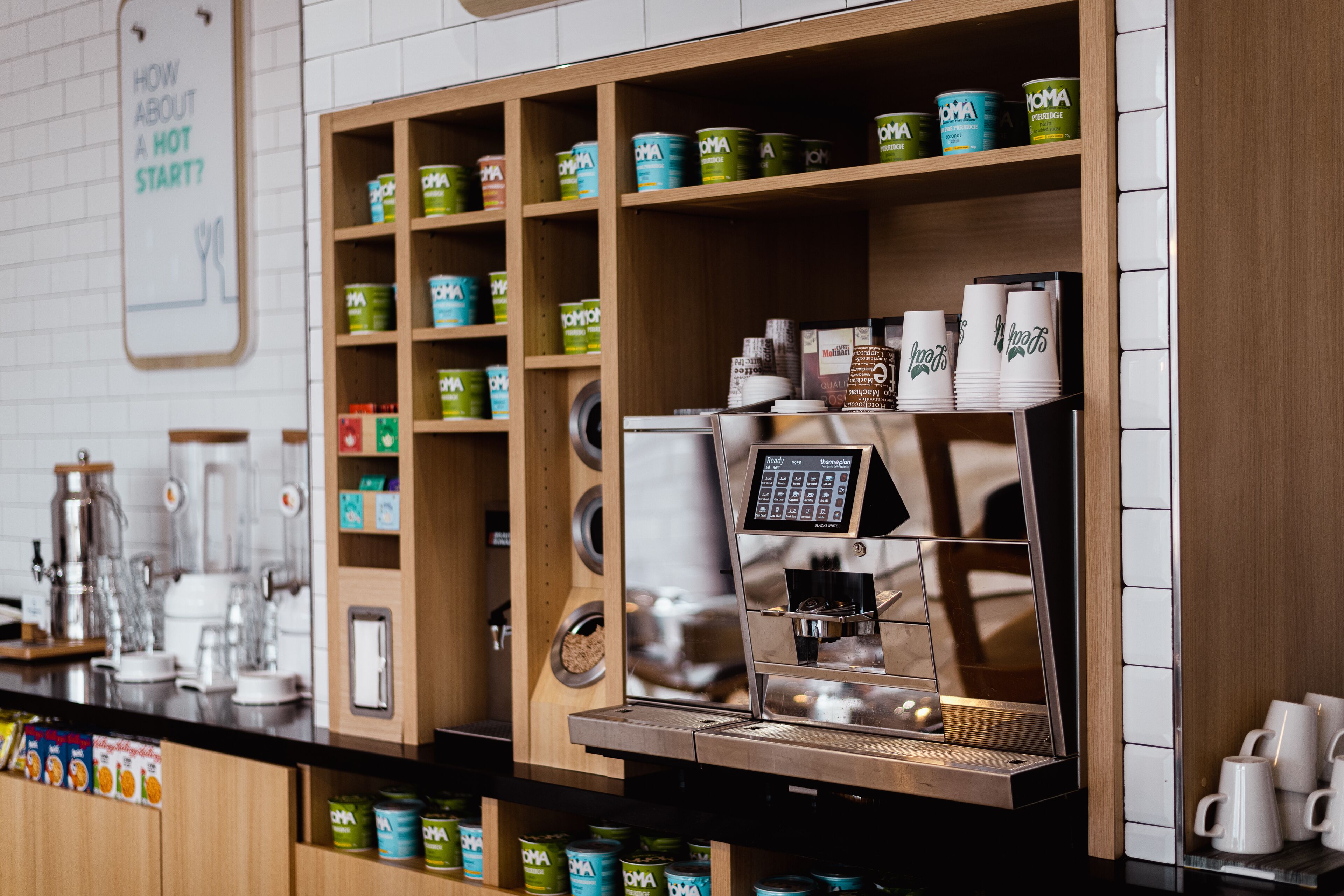 L’intérieur d’un café, avec une machine à café, des étagères remplies de conserves et un panneau accroché au mur.
