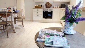 A modern kitchen with white cabinetry, a heart-shaped vent, and a dining area with a table set for two. - Linton Court Coach House (Settle)