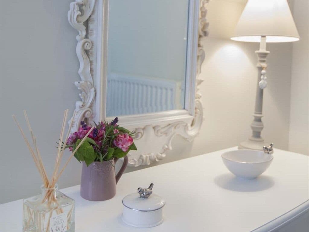 Un mobile bagno con un piano di lavoro bianco, una bacinella bianca, un piccolo contenitore e un vaso con fiori.