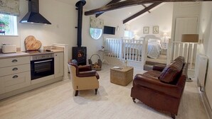 A cozy living room with a fireplace, a dining area with a wooden table, and a kitchen with modern appliances. - Linton Court Coach House (Settle)
