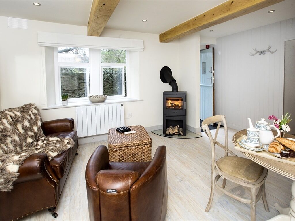 Un salon chaleureux avec une cheminée, des meubles en cuir, une table à manger avec un service à thé, et une vue sur l’extérieur.