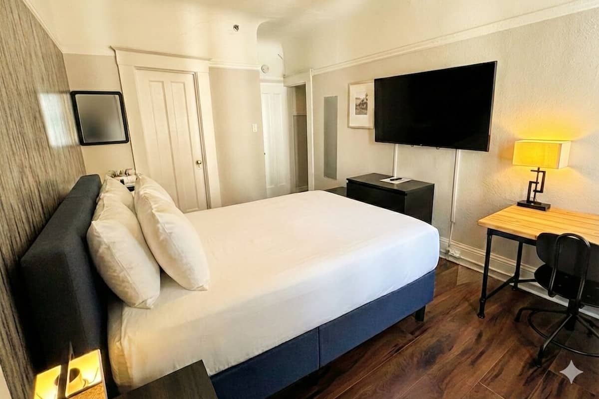 Una habitación de hotel con cama, escritorio, silla, televisor y lámpara.