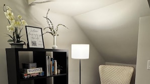 A cozy reading nook with a bookshelf, a chair, and a floor lamp in a room with sloped ceilings. - Hotel Ikon (San Francisco)