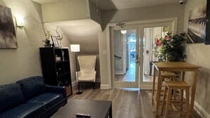 A living room with a dark-colored sofa, a coffee table, a bookshelf, a white armchair, and a wooden table with chairs. - Hotel Ikon (San Francisco)