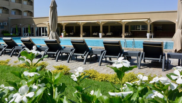 Zona junto a la piscina con sillas de descanso y sombrillas, una piscina y un edificio con varios pisos y balcones.