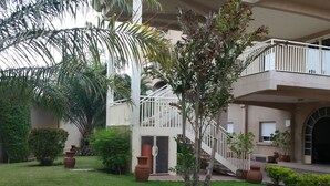 Un edificio de varios niveles con una escalera central, rodeado de céspedes cuidados y diversas plantas en macetas.