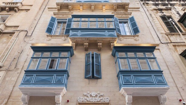 Fachada de edificio con varias ventanas, algunas con contraventanas y molduras decorativas.