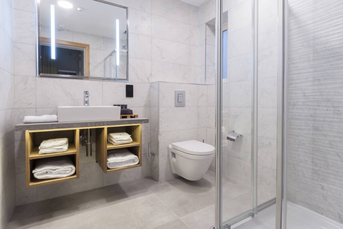 Ein modernes Badezimmer mit Marmorwaschbecken, Holzregalen, Toilette und einer Duschkabine aus Glas.