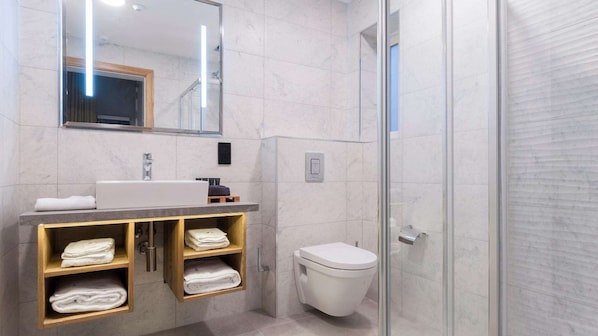 Un baño moderno con un lavamanos de mármol, cabina de ducha de vidrio y estantes de madera con toallas.