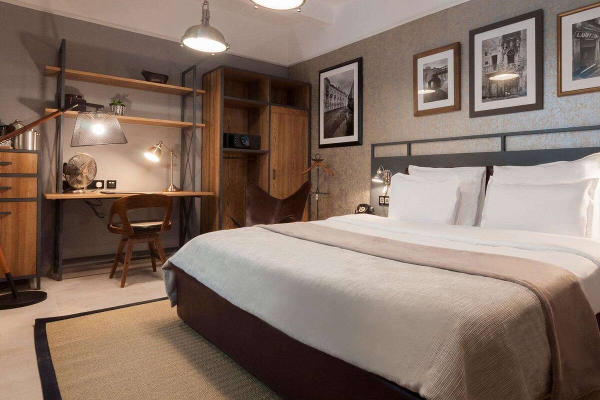 Ein Schlafzimmer mit einem großen Bett, einem Schreibtisch und Regalen. An der Wand hängen gerahmte Bilder.