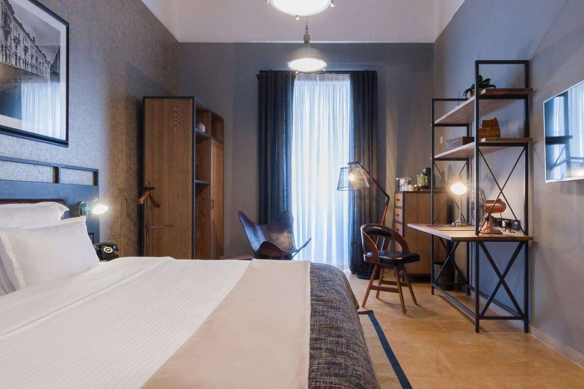 Ein modernes Hotelzimmer mit einem großen Bett, einem Schreibtisch mit Stuhl, einem Kleiderschrank und einem Spiegel an der Wand.