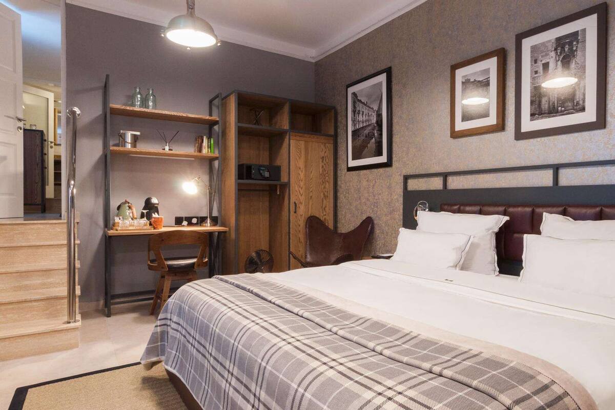 Ein Hotelzimmer mit einem großen Bett, einem Holztisch mit Stuhl, einem Bücherregal und gerahmten Bildern an der Wand.