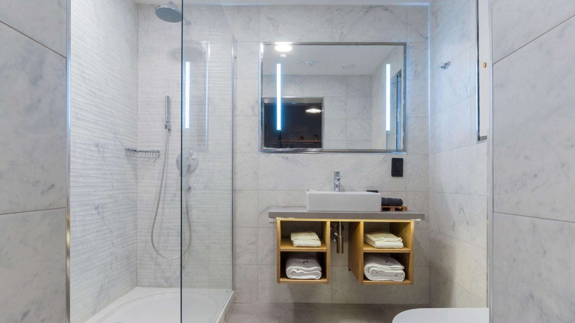 A modern bathroom with a glass-enclosed shower, a large mirror, and a wooden vanity with shelves for towels.