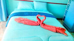 Ein Bett mit einer blau-weißen Tagesdecke und einem roten Handtuch, das zu einem Herz geformt ist.