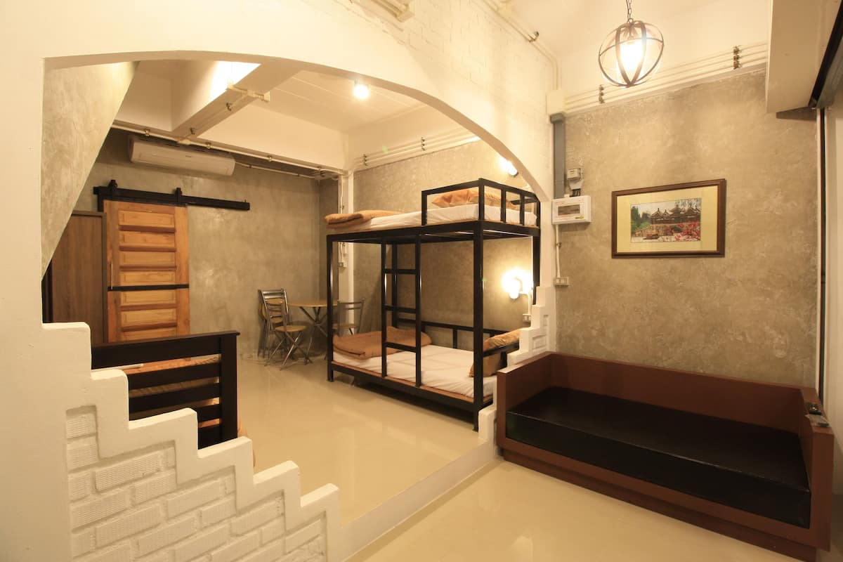 A room with bunk beds, a wooden bench, a staircase, and a framed picture on the wall.