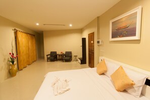 A hotel room with a bed, two chairs, a small table, a vase with flowers, and a painting on the wall. - Sirin House (Krabi)