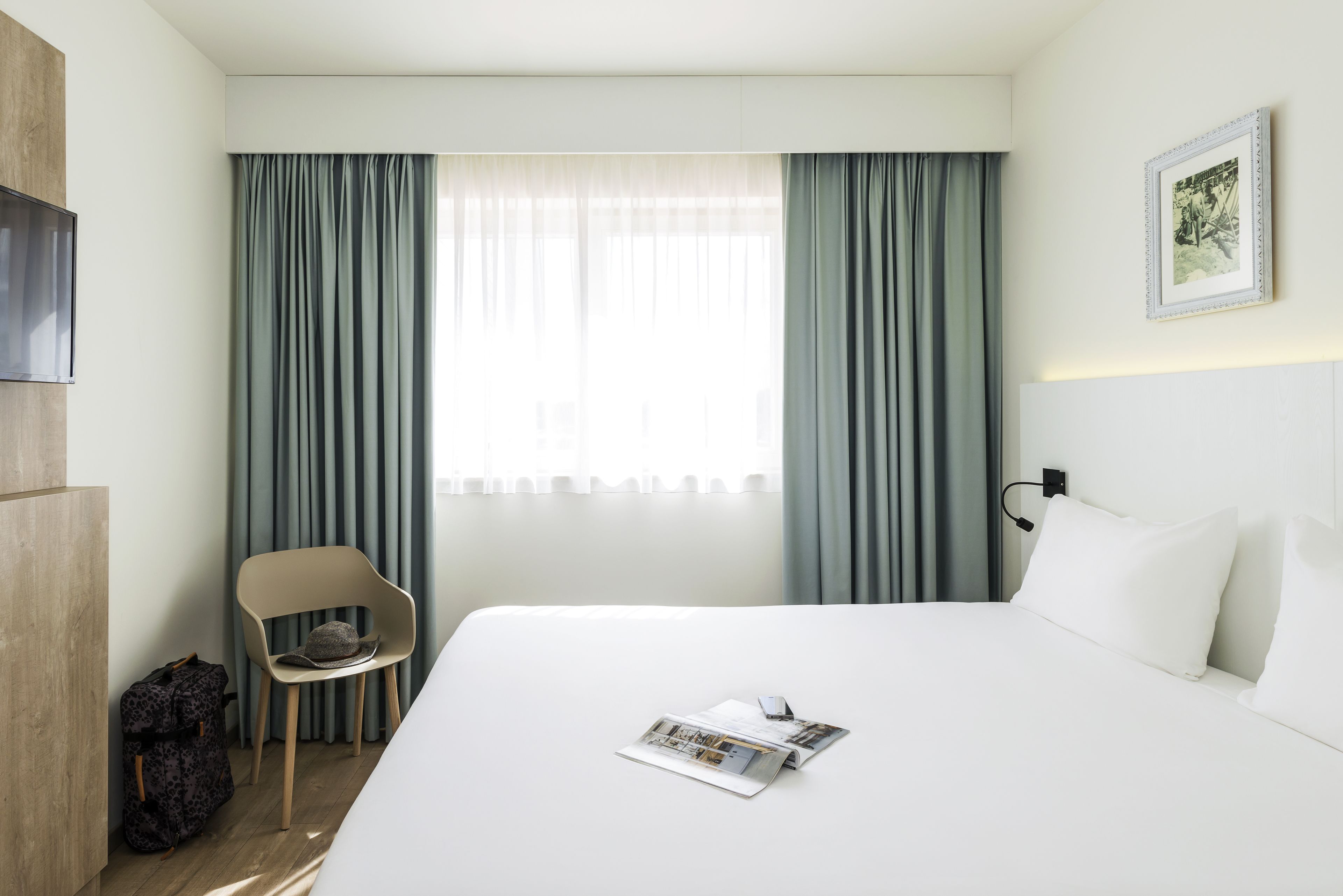 Ett hotellrum med en säng, en stol, ett skrivbord och en tv.