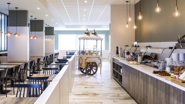 A modern cafe with a central serving counter, seating area, and a view of the street.