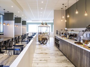 A modern restaurant with a central serving counter, seating area, and a view of the cityscape. - ibis Styles Nieuwpoort (Nieuwpoort)