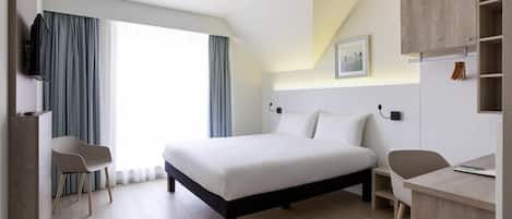 A modern hotel room with a large bed, two chairs, a desk, and a TV.