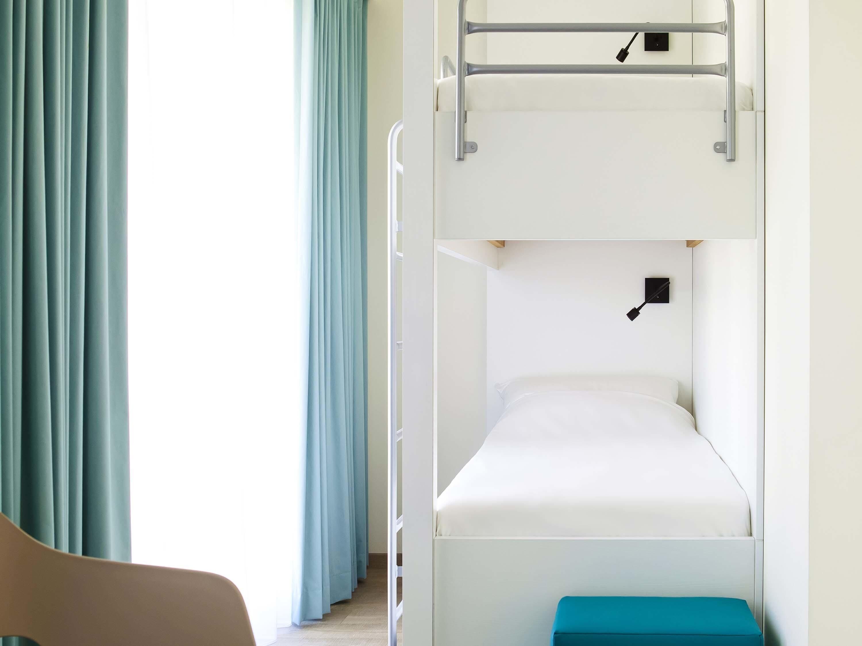 Een slaapkamer met stapelbed, raam, gordijnen, bureau en stoel.