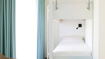 Een slaapkamer met stapelbed, raam, gordijnen, bureau en stoel.