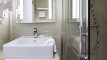 A modern bathroom with a large sink, a glass shower enclosure, a towel dispenser, and a hairdryer.